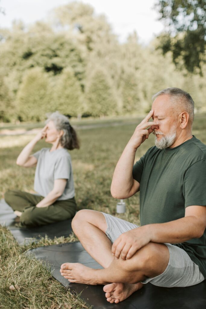 A couple, two old persons breathing on a green grass surrounded by lush greenery and sunlight.